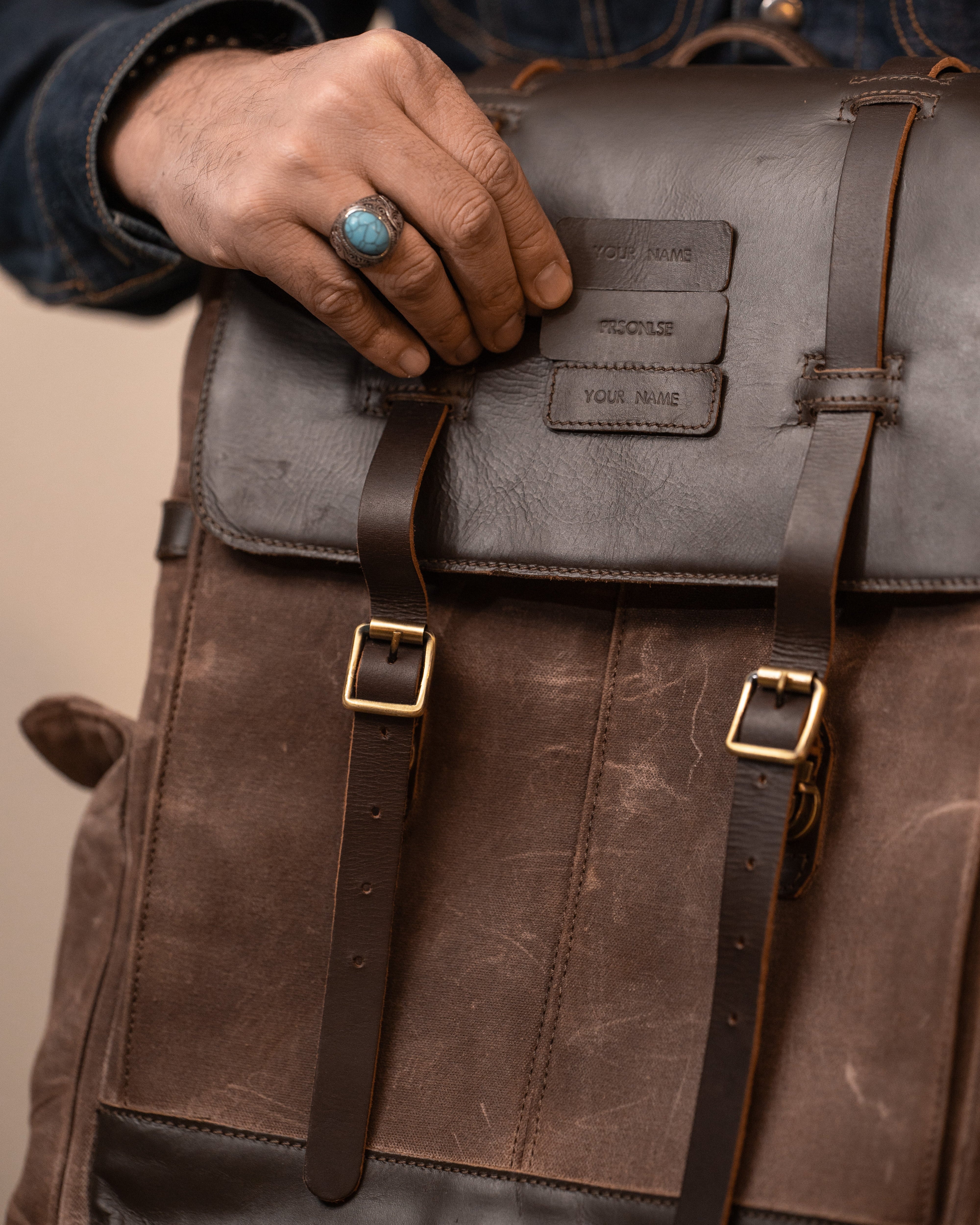 Person holding a leather backpack with visible branding