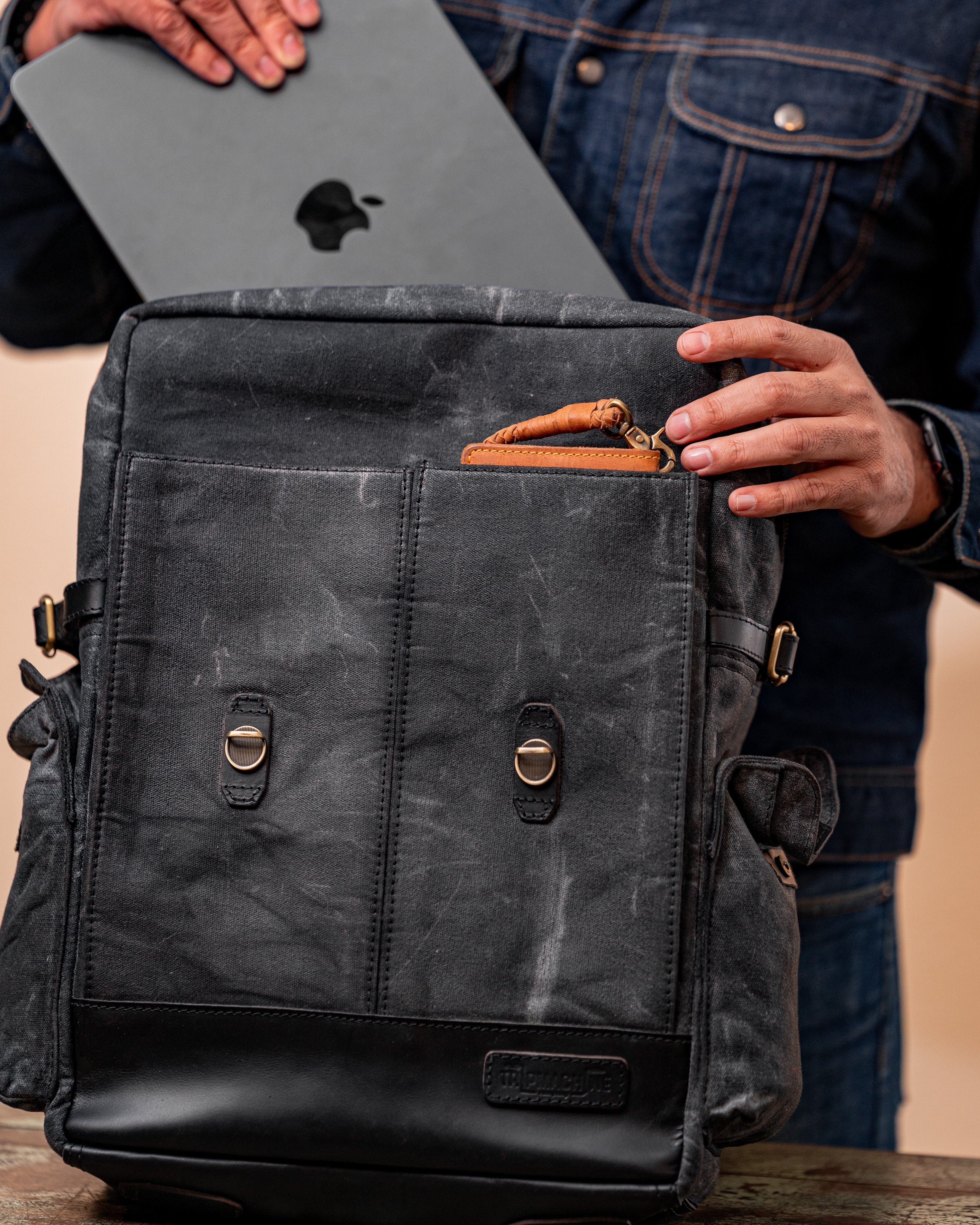 Person holding a gray laptop above a black backpack on a wooden surface.