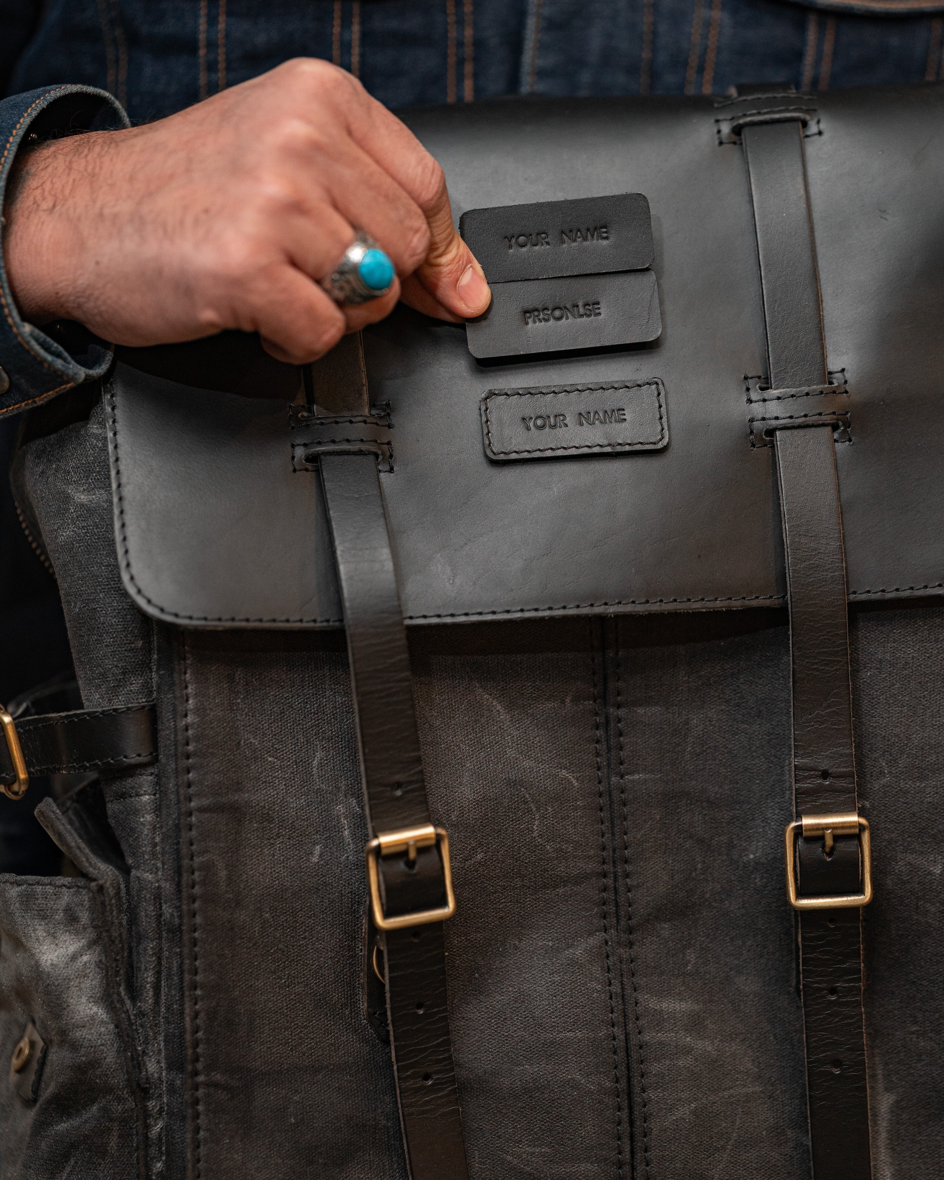 Person holding a black leather backpack with visible branding.