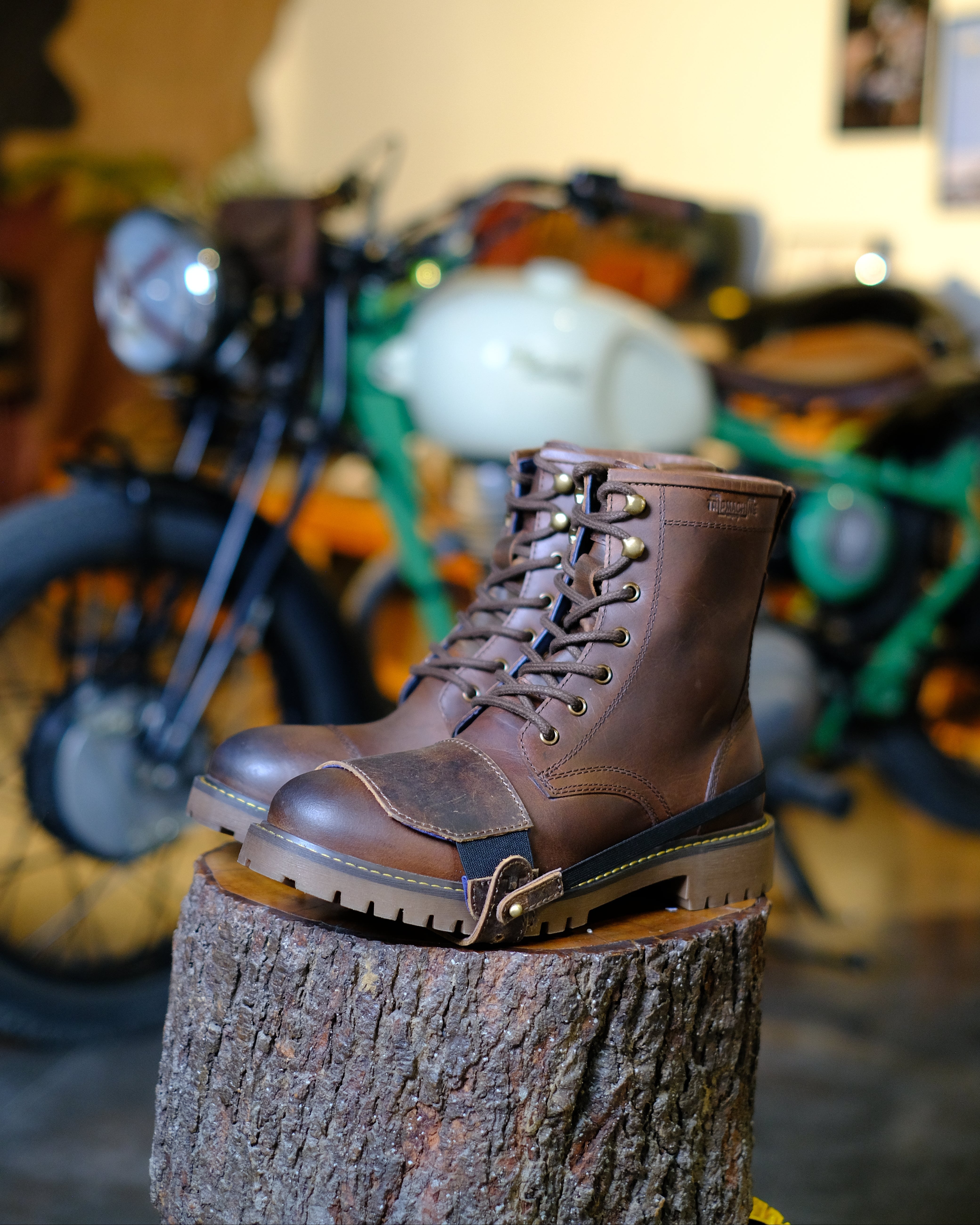 Brown leather boot with mocha shoe protector on a tree stump with a motorcycle in the background