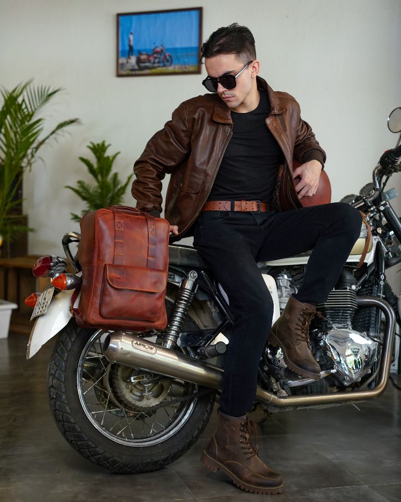 A man is seated on motorcycle with handmade genuine leather cherry red color eastwood backpack mounted on a bike