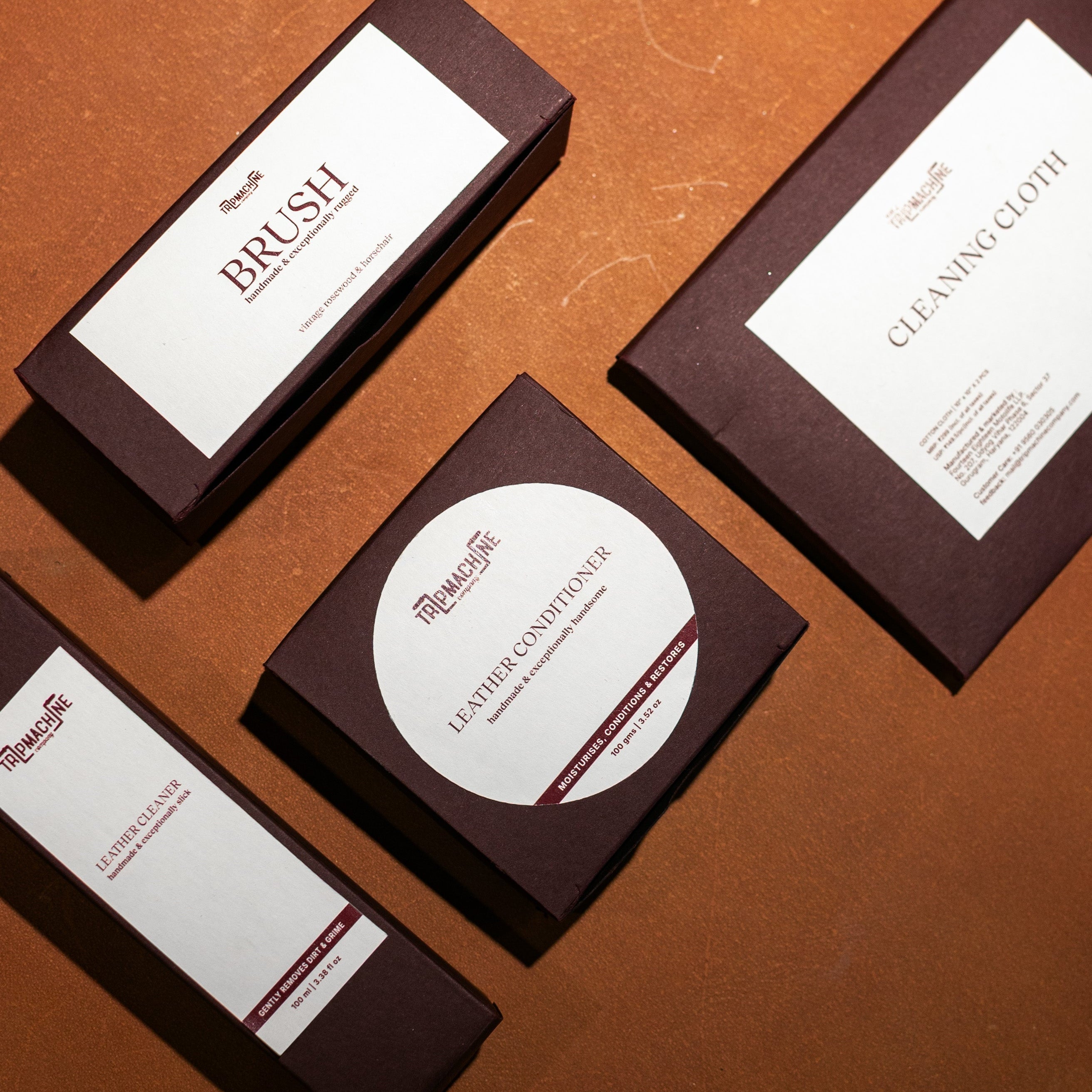 Set of leather care products including a brush, cleaning cloth, and leather conditioner on a brown surface.
