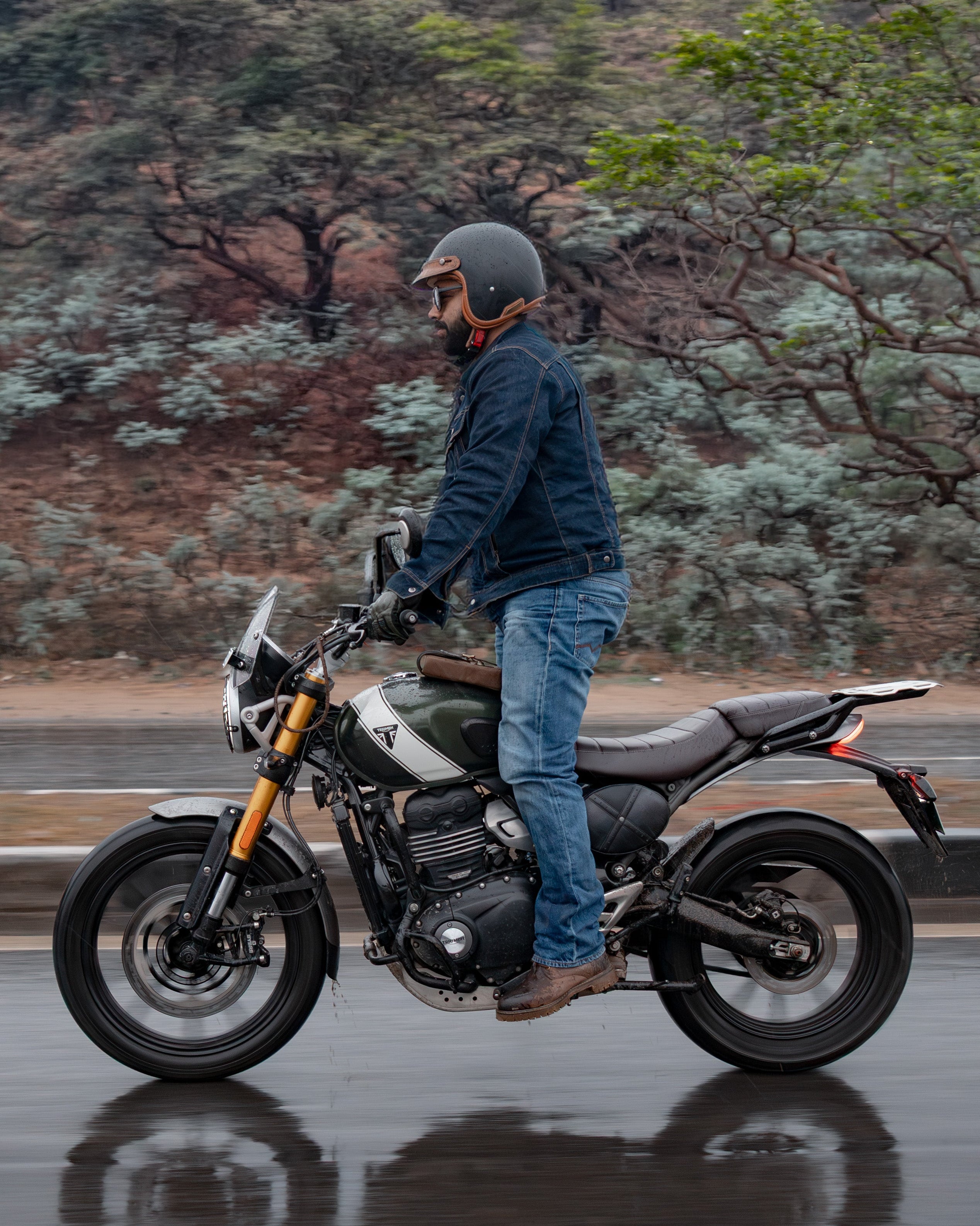 Person standing next to a motorcycle on a wet road with a forested background