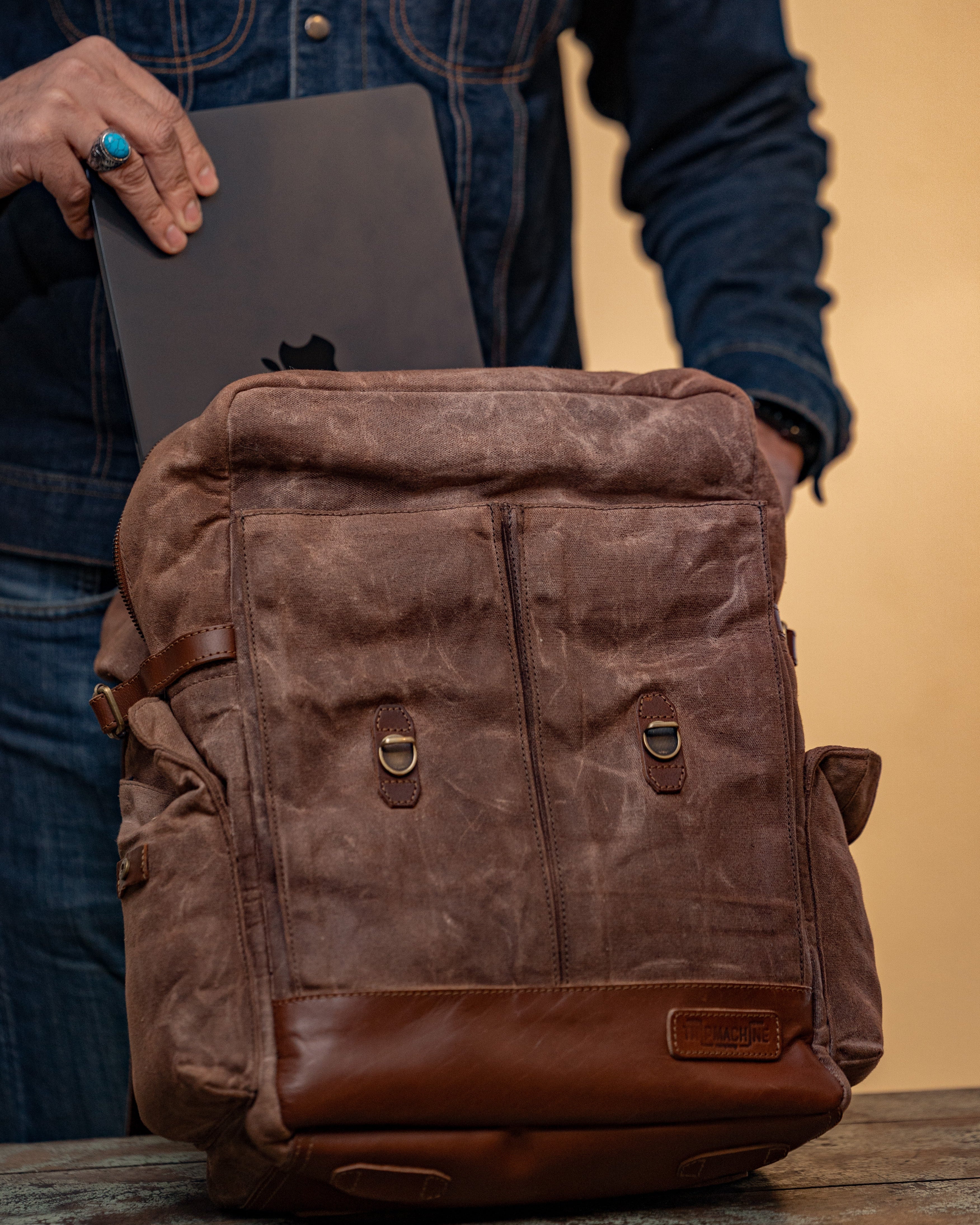 Person holding a brown leather backpack with a plain background