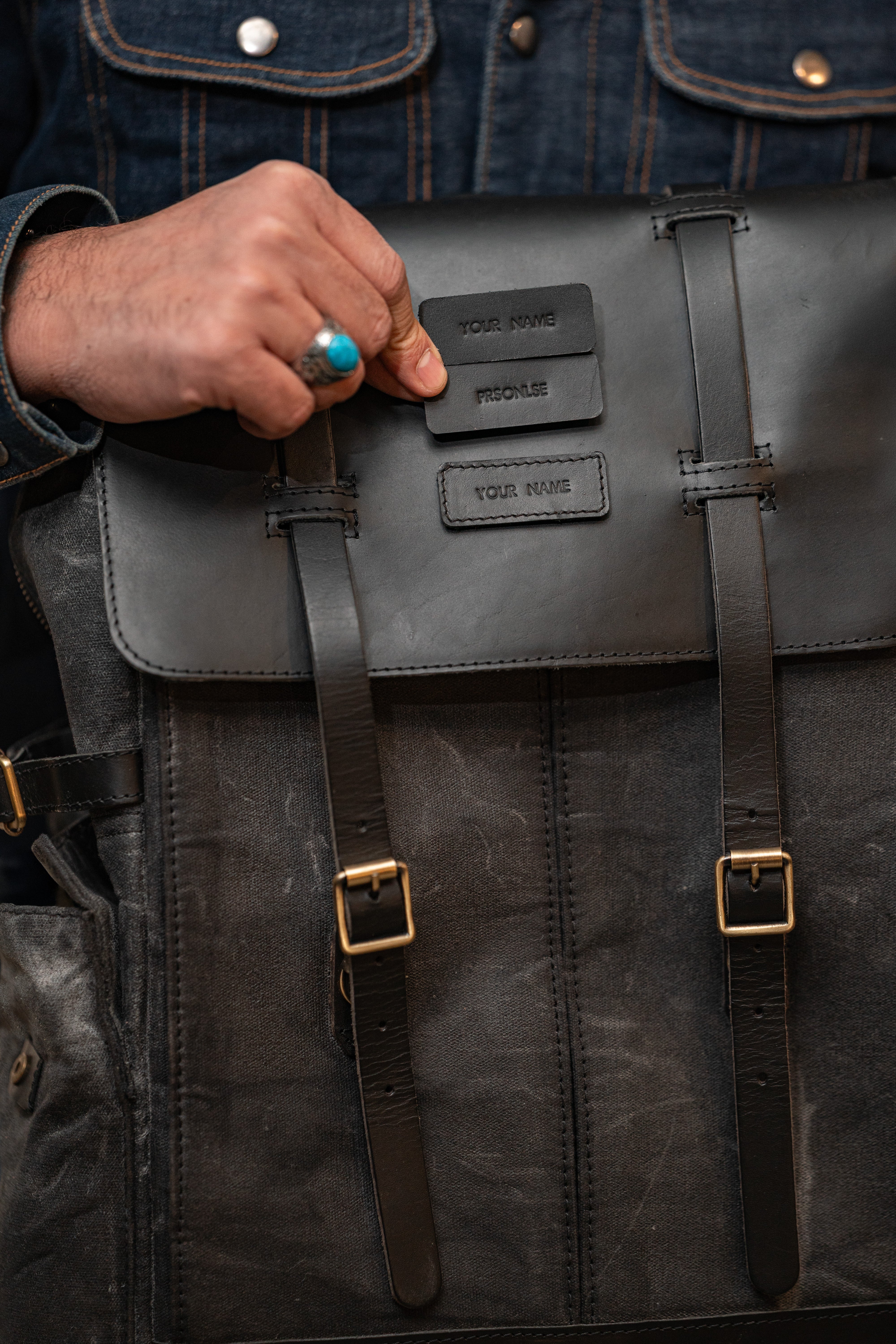 Person holding a black leather backpack with visible branding.