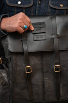Person holding a black leather backpack with visible branding.