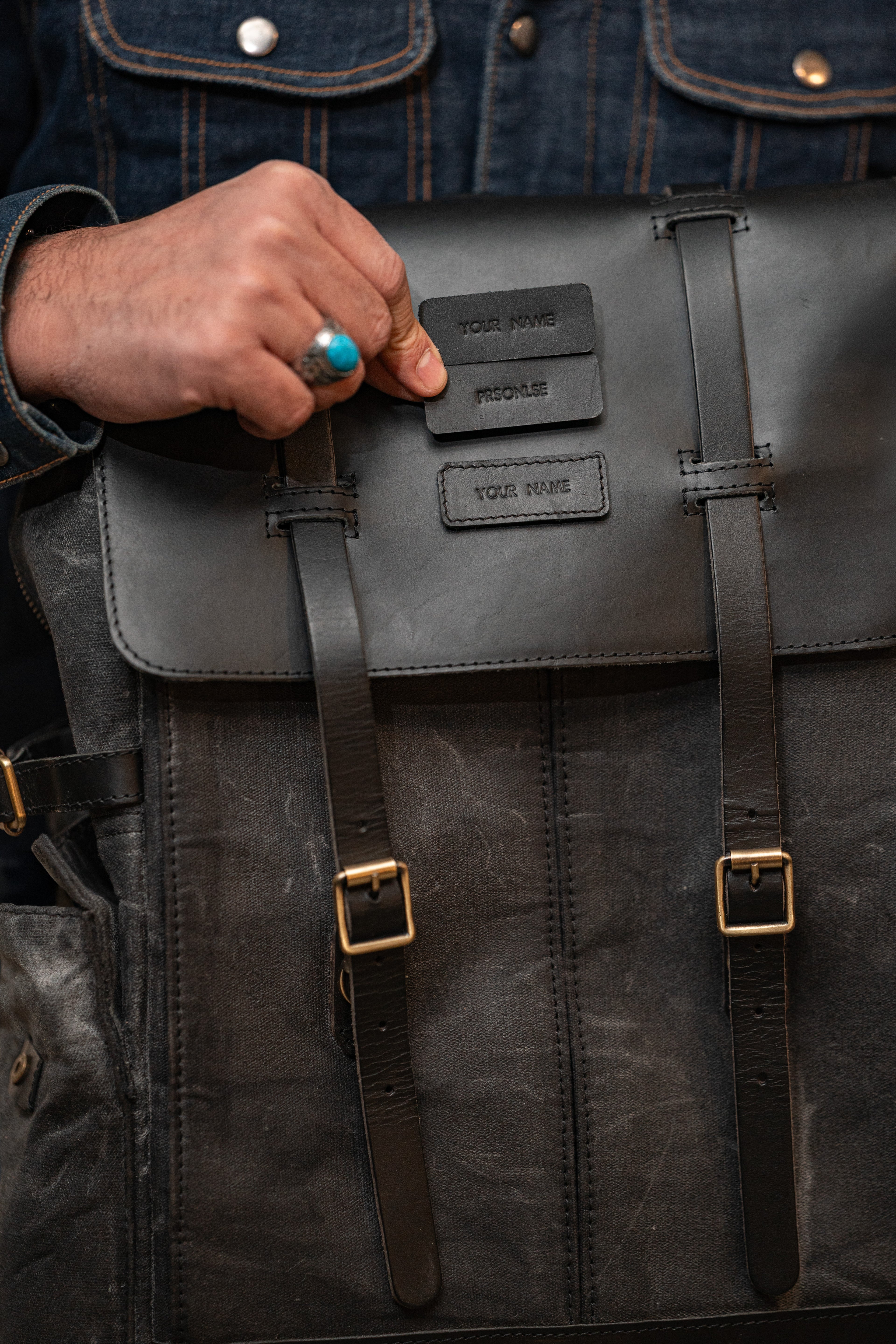 Person holding a black leather backpack with visible branding.