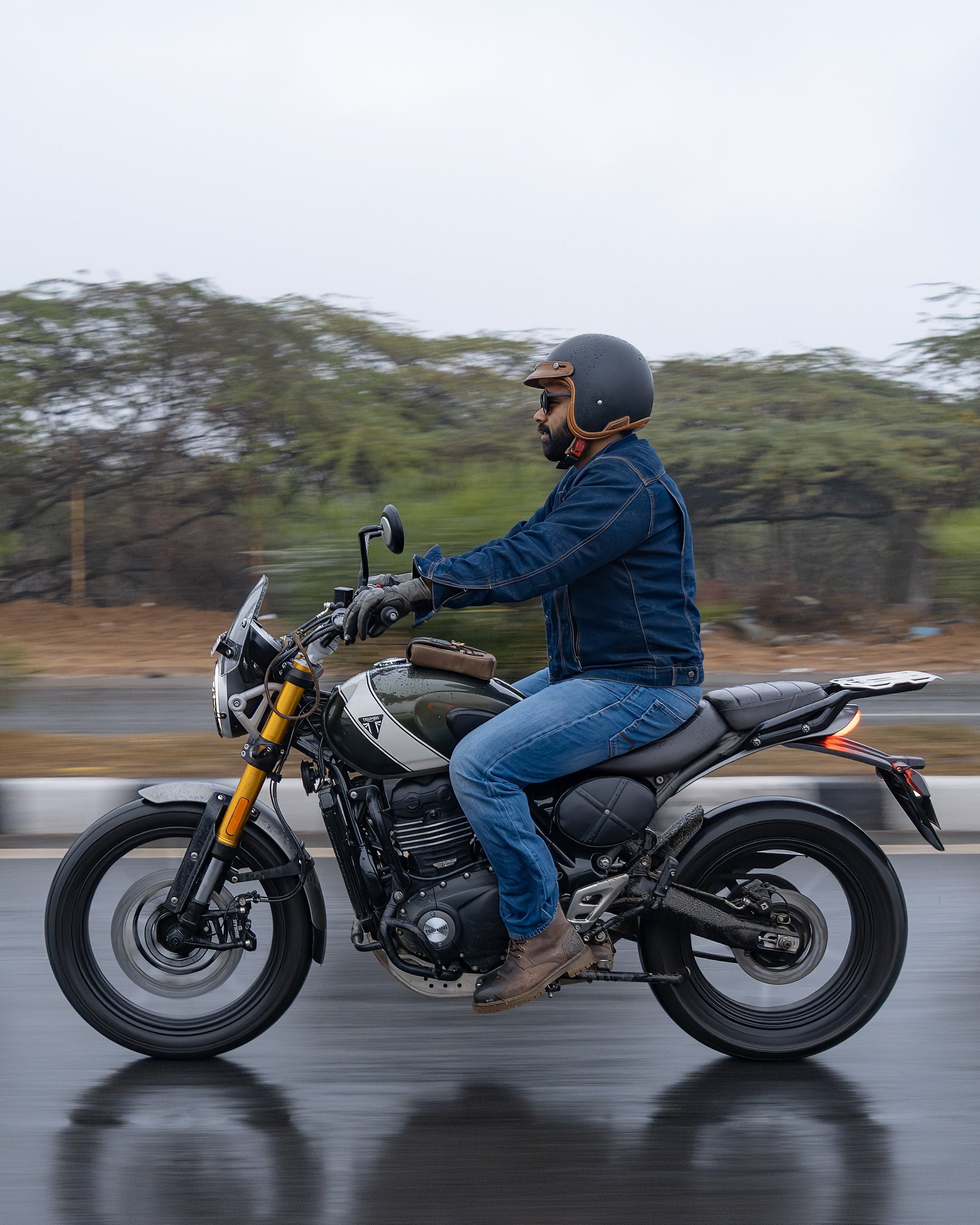 Person riding a motorcycle on a wet road with trees in the background