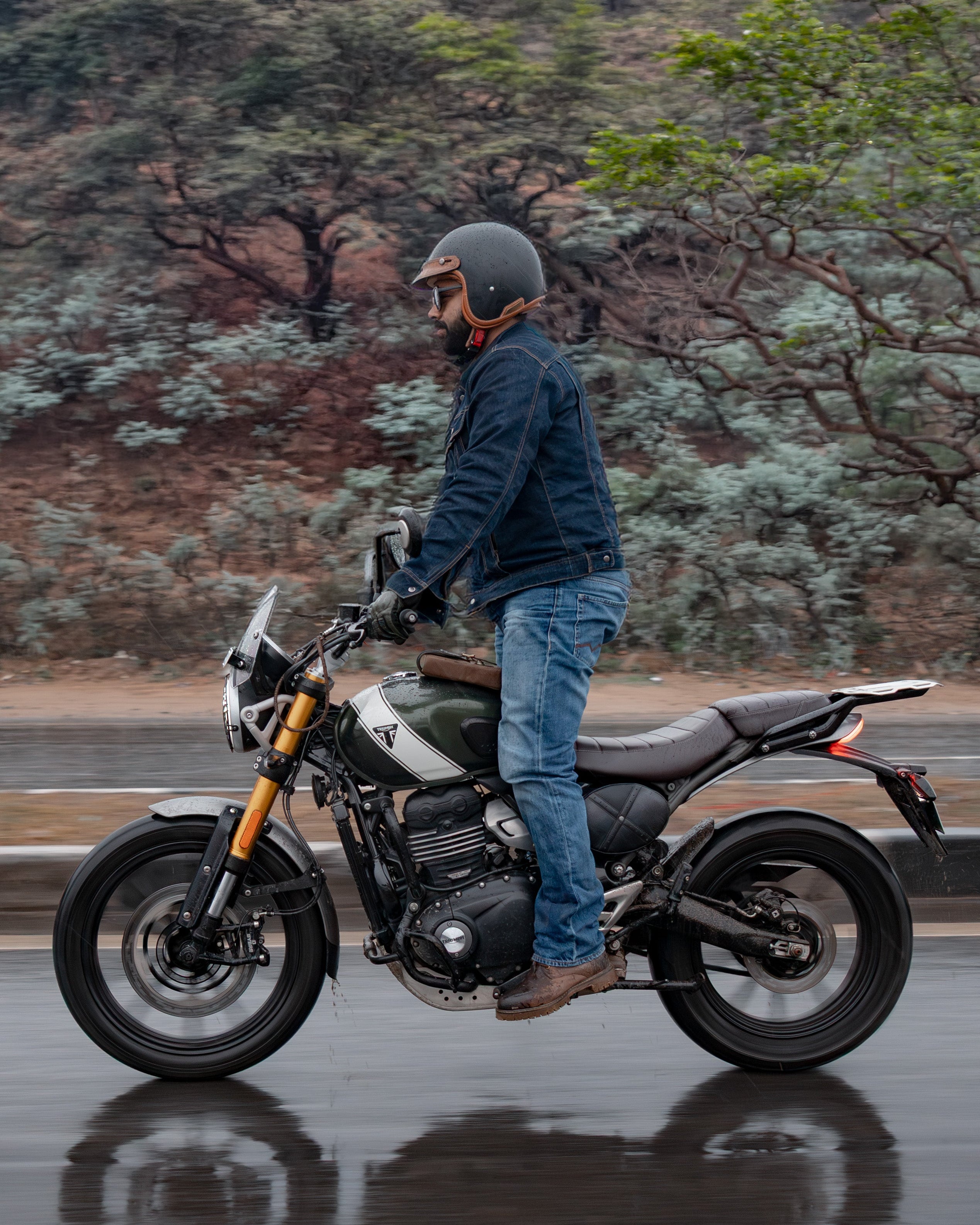Person standing next to a motorcycle on a wet road with a forested background