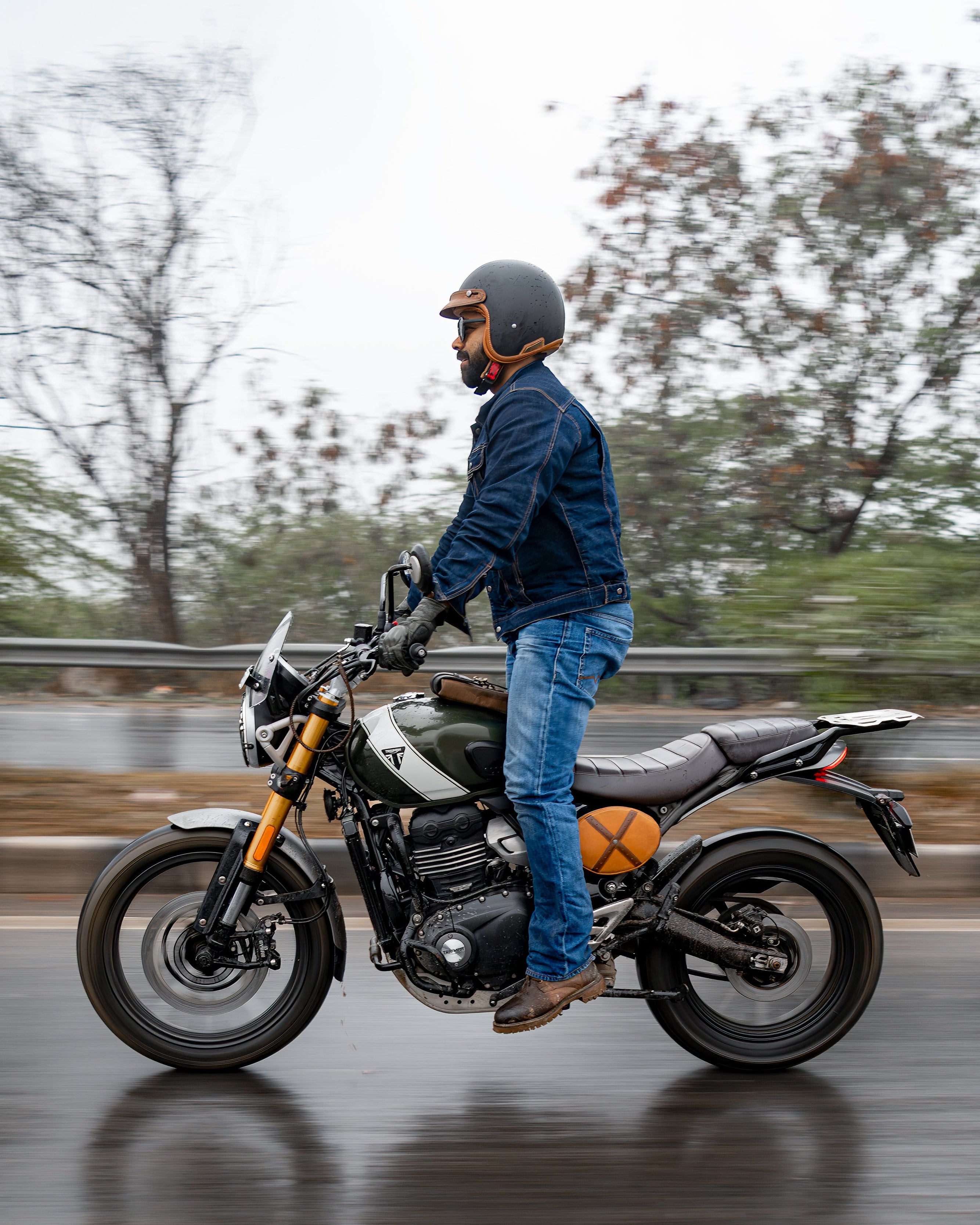 Person on a motorcycle on a wet road with trees in the background